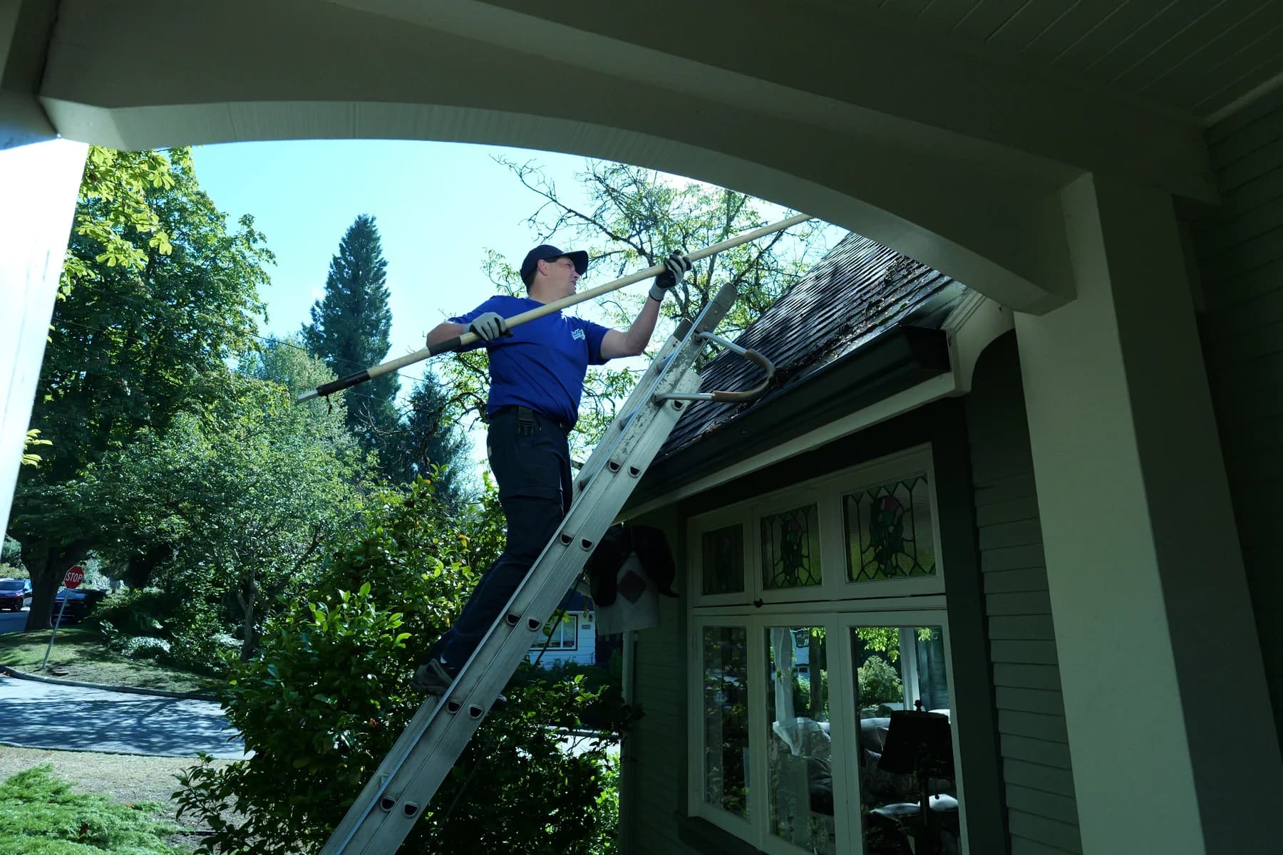 A Holland Home Services technician on a ladder clearing a gutter on a Vancouver home